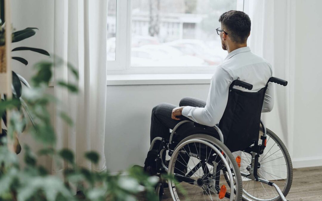 Man in wheelchair gazing out window indoors.